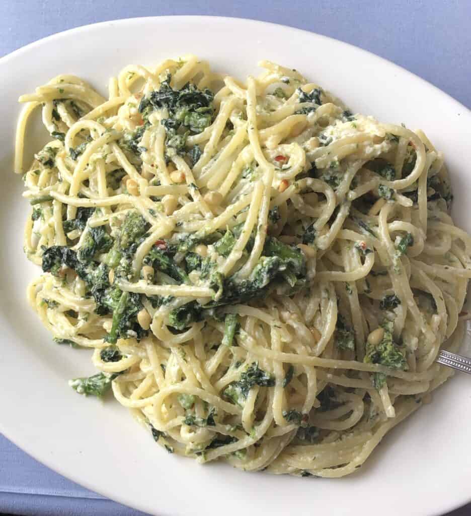 Delicious creamy spinach pasta with herbs and cheese on a white plate.